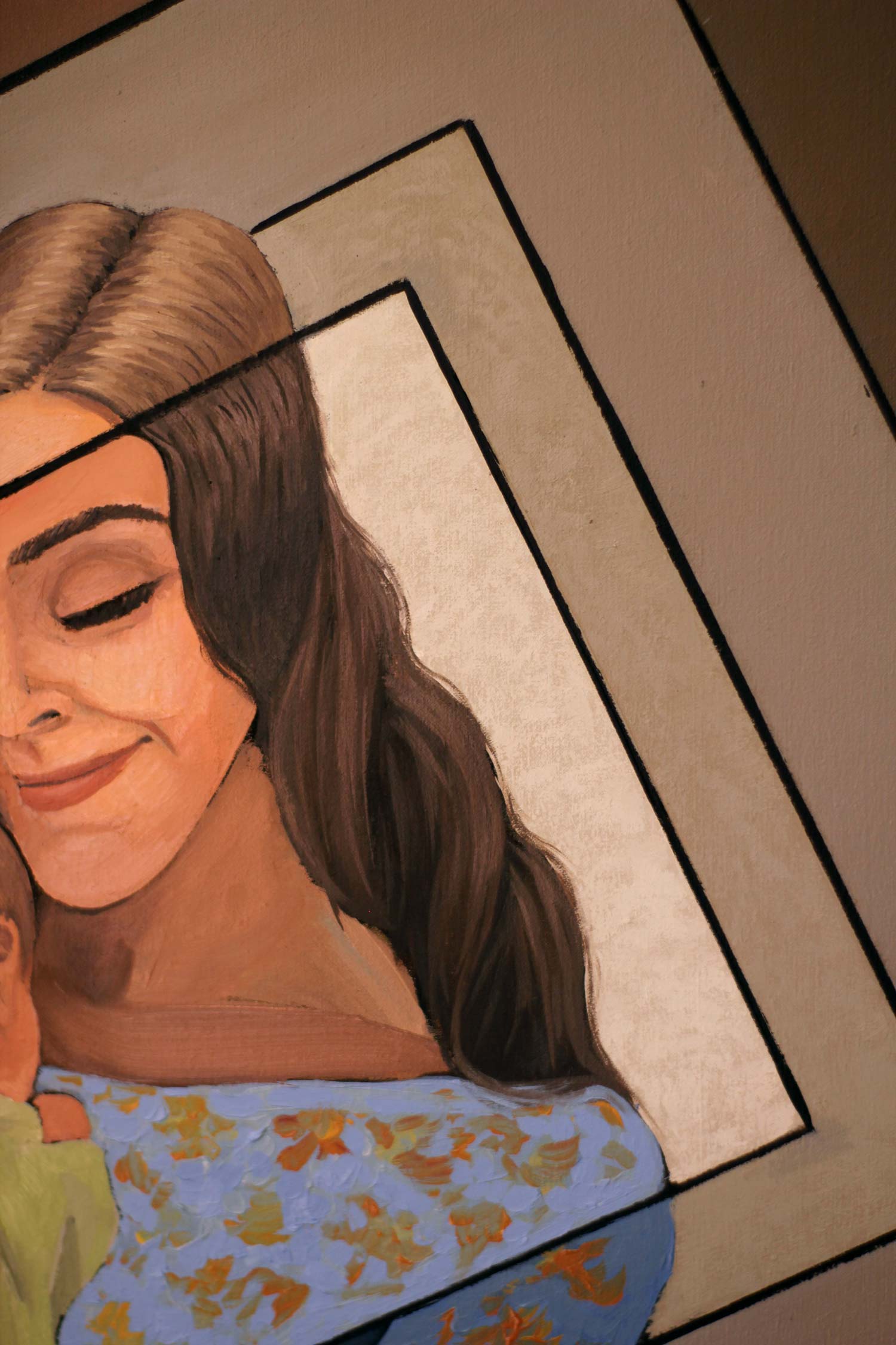 Close-up of the mother's serene face with closed eyes and a gentle smile, framed by flowing dark hair and intersecting geometric lines.